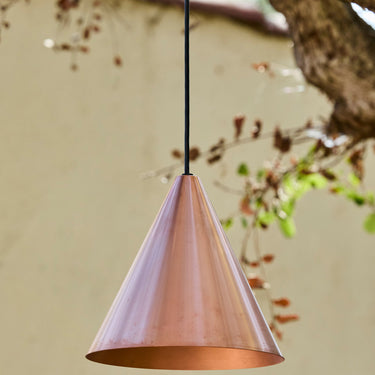 Copper tratten jakobsson pendant light hanging against a neutral background with foliage.