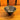 A small handmade Carl Auböck metal bowl with a dark textured interior and a polished gold-toned rim, resting on a wooden table with a wooden chair back in the background.