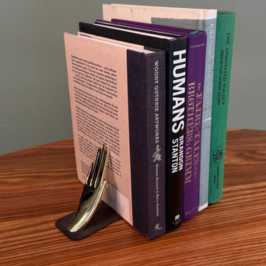 Set of books with a brass hand-shaped bookend on a wooden surface