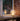 A modern table lamp with a translucent spherical shade and glowing warm bulb sits on a windowsill in a cozy interior beside a brick wall and books.