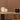 Modern desk setup with a laptop, plant, and decorative lamps against a wooden wall.