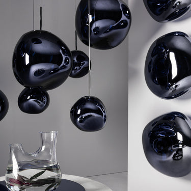 Black spherical hanging lights in a modern interior setting with a clear vase on a table.