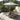 Wooden lounge chair under a large umbrella on a stone patio with trees in the background