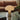 Mushroom-shaped lamp on a glass table with a brown sofa and plant in the background
