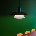 Modern black pendant light over a dining table with chairs against a green wall