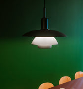 Modern black pendant light over a dining table with chairs against a green wall