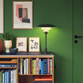 Bookshelf against a green wall with books, a lamp, and framed pictures.