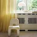 White chair in a room with yellow curtains and a radiator.