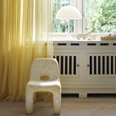 White chair in a room with yellow curtains and a radiator.