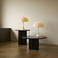 Two table lamps on black round tables against a plain wall.