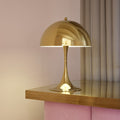 Gold or brass 70s table lamp on a wooden surface with a pink curtain in the background