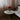 Round white table with a red lamp and books in a room with curtains and a sofa.