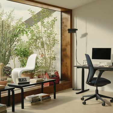 Modern home office with a desk, chair, and computer setup near a large window with plants.