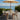 Outdoor dining set with table and chairs under a large striped umbrella by the sea.