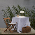 Table setting with a lamp and basket on a wooden platform by a body of water.