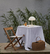 Table setting with a lamp and basket on a wooden platform by a body of water.