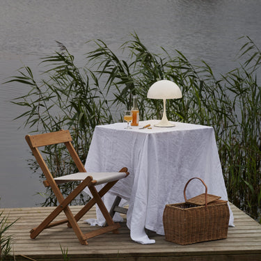 Table setting with a lamp and basket on a wooden platform by a body of water.
