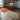 A styled dining room corner featuring a wooden dining table and chairs, wall-mounted wooden shelves, a black floor lamp, and three organic-shaped area rugs on a light wood parquet floor.