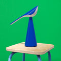 Blue bird-shaped lamp on a wooden stool against a green background
