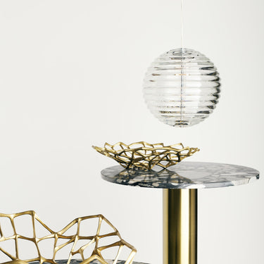 Decorative gold bowl and marble side table with a white background and pressed glass round pendant from tom dixon