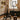 Modern interior with gold pendant lights, black chair, and decorative table in a room with brick walls and large window.