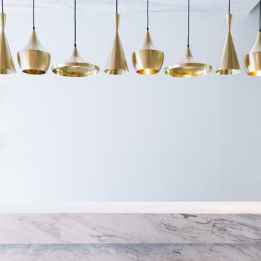 Gold pendant lights hanging above a marble countertop with black stools.