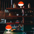 Two orange-lidded lamps on a green counter with shelves in the background