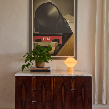 V3253 pale yellow conica table lamp artemide lit on midcentury credenza with a plant
