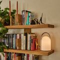 Wooden bookshelf with books, a lamp, and candles against a beige wall.