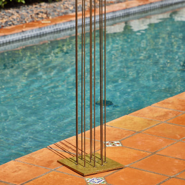 Metal bertoai sculpture with vertical rods on a tiled poolside area