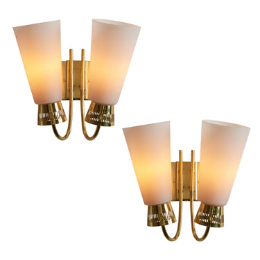 Two gold wall sconces with white lampshades on a white background