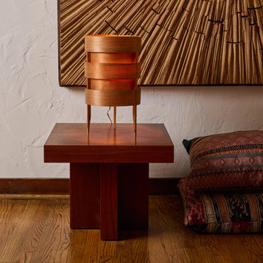 Wooden lamp on a table with a textured wall and patterned pillow in the background