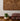 Wooden wall art with concentric circle design on a white wall, with a plant and cushion in the foreground.