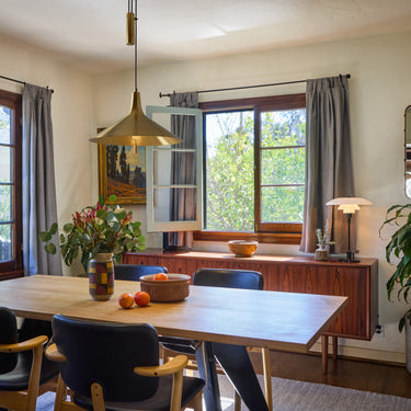 brass pendant in Dining room with wooden prouvé table, chairs, and large windows.