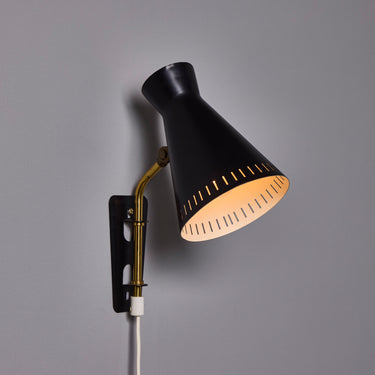 Black wall-mounted lamp with gold interior on a gray background Black wall-mounted midcentury diabolo shaped lamp with plug and brass arm by Mauri Almari on a white background