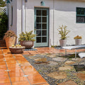 Outdoor patio with tiled and stone pathways, potted plants, and a white building with green door.