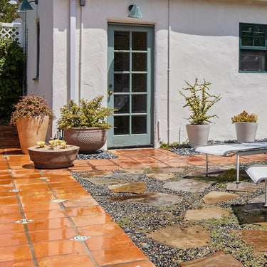 Outdoor patio with tiled and stone pathways, potted plants, and a white building with green door.