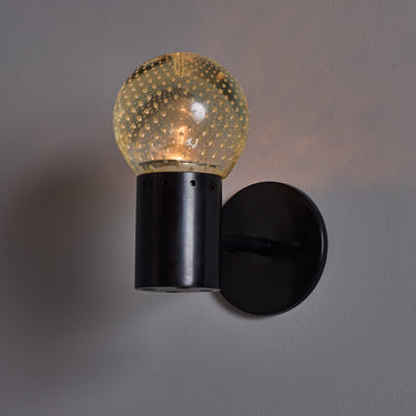 Black wall-mounted light fixture with a textured glass shade on a gray background