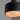 Close-up of a modern pendant light with a matte black cylindrical shade and a glowing warm white spiral diffuser, suspended against a plain gray background.