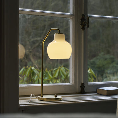 Table lamp with a warm glow on a windowsill with a view of greenery outside.