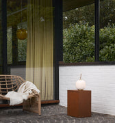 Modern outdoor patio with wicker chair, hanging light, portable glass light and side table.