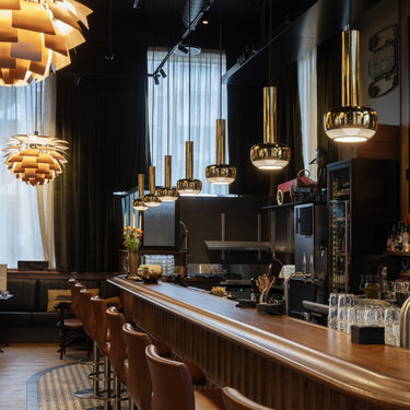 Modern bar interior with wooden counter, chairs, and stylish brass lighting fixtures.