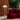 A modern curved magenta-red upholstered sofa in a stylish interior, next to a tall silver wire floor lamp with a white globe shade, set against a brown slatted wood wall and a large green potted plant.