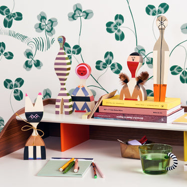 Desk with decorative wood dolls by Alexander Girard against a wallpapered wall