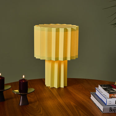 Yellow geometric table lamp on a wooden surface with books and candles