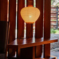 Woven lamp on a wooden table with wooden slatted wall and outdoor view in the background