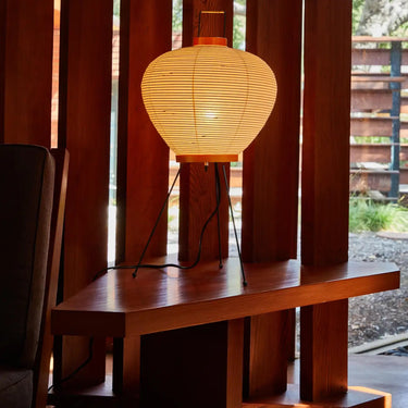 Woven lamp on a wooden table with wooden slatted wall and outdoor view in the background