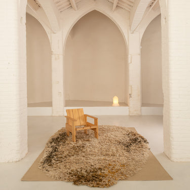 Wooden chair on a textured rug in a room with high arched ceilings and white walls.