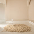 Beige deep shag rug on a light wooden floor with a white jean prouvé chair against a beige wall.