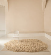 Beige deep shag rug on a light wooden floor with a white jean prouvé chair against a beige wall.